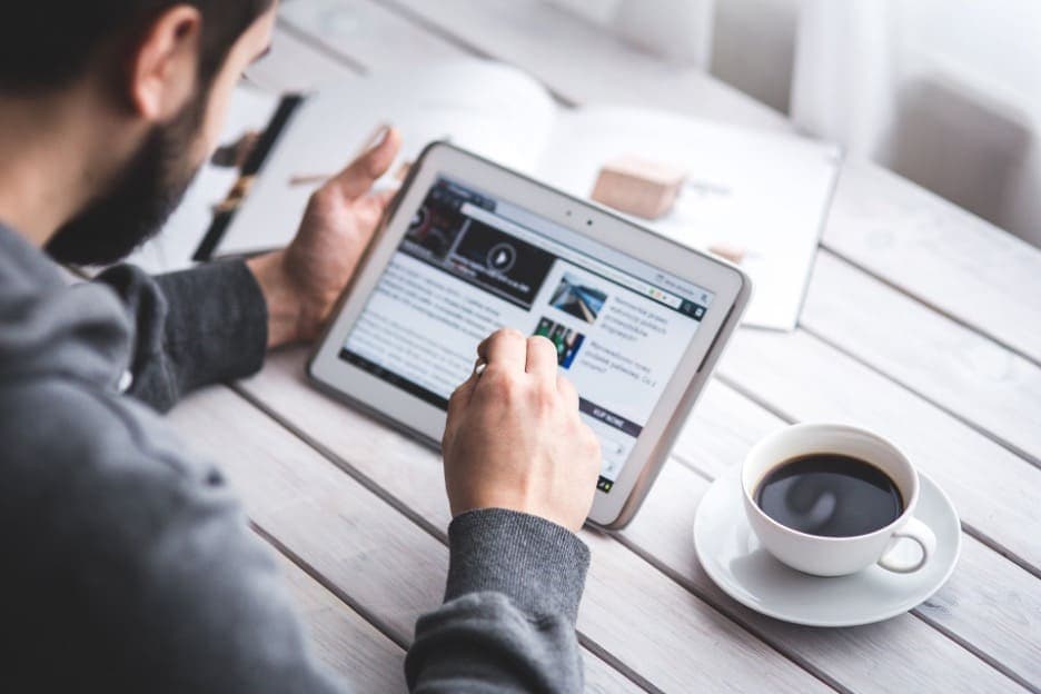 Person reading content on a tablet at a desk with coffee — researching B2B lead generation strategies